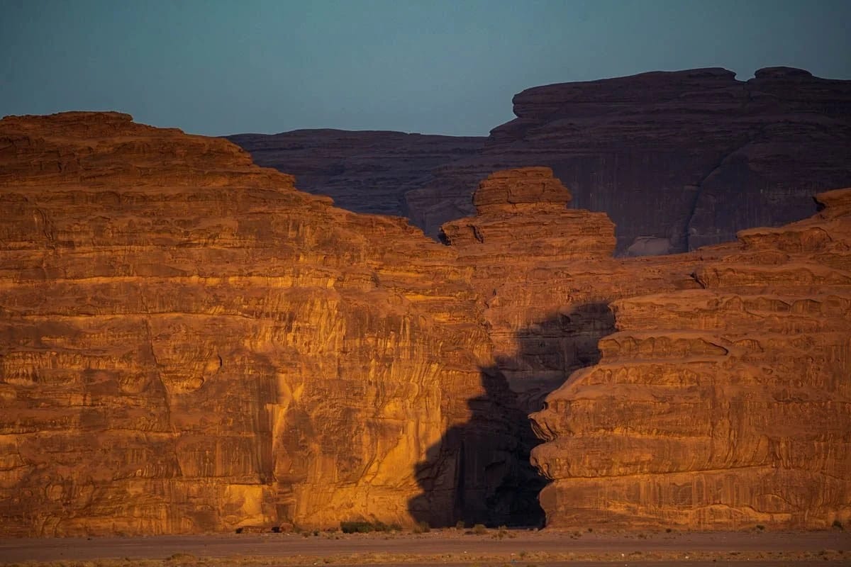 A red sandstone cliff split by a narrow canyon under a deep blue sky.