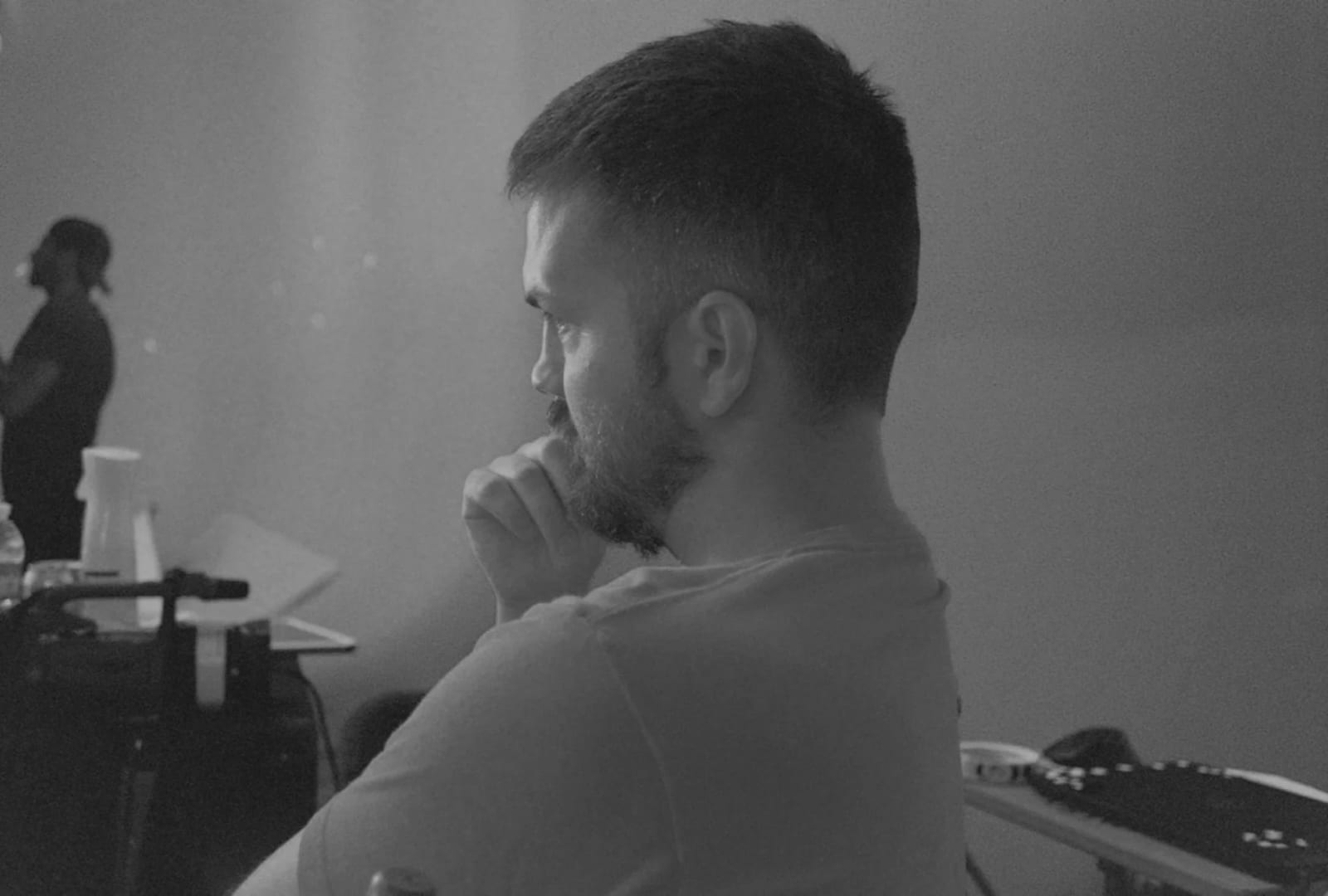 Black and white photograph of Ryan Staake in a white T-shirt seen from behind at a desk, hand at his chin.