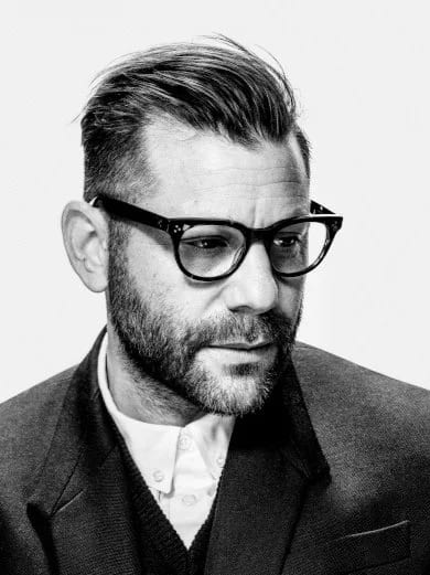 Black and white portrait of Anthony Mandler, bearded, in thick-rimmed glasses and a suit jacket, looking off to the side.