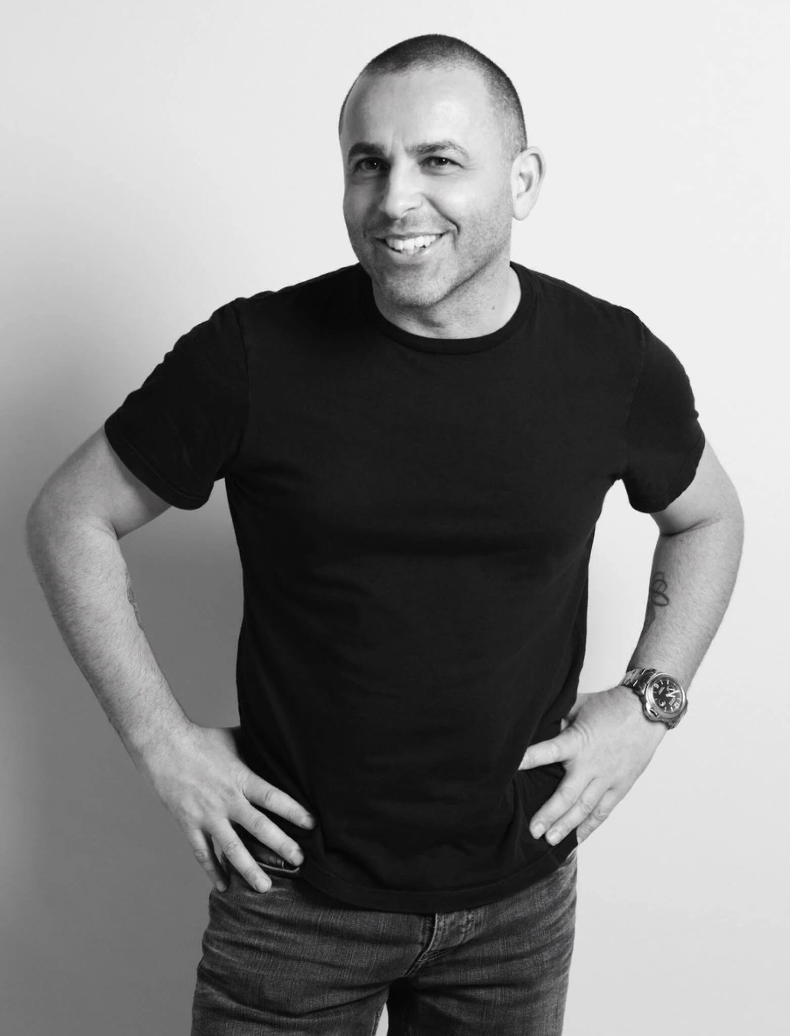 Black and white photograph of Lorenzo Agius smiling in a black T-shirt with his hands on his hips.