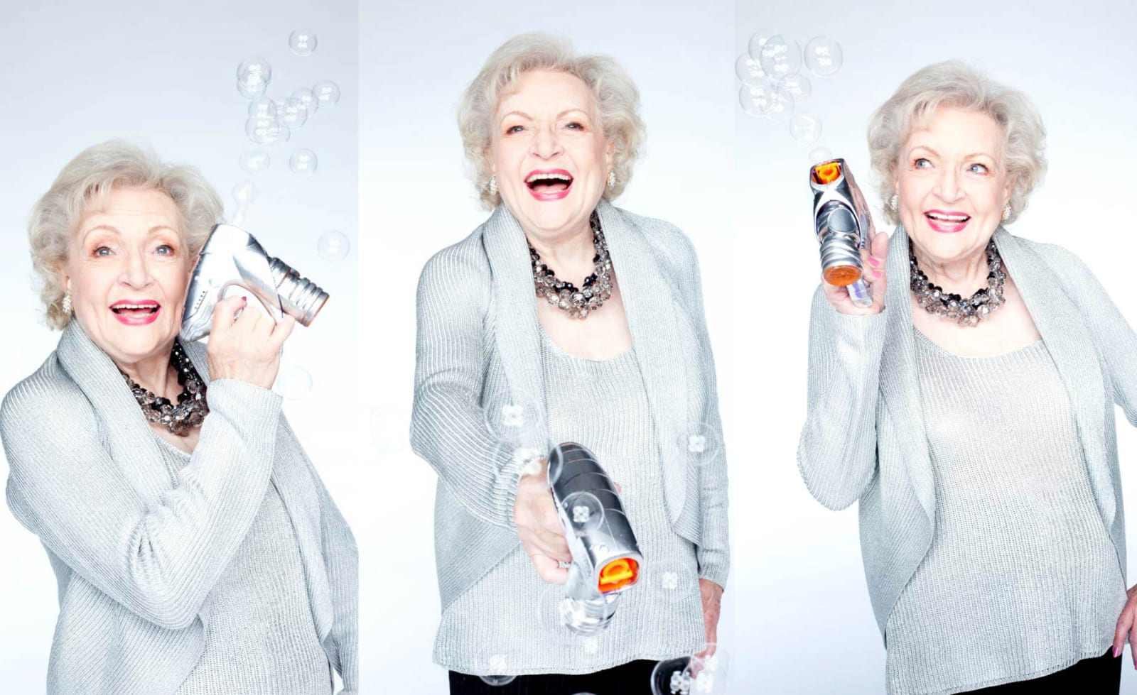 Three studio shots of a white-haired woman in a grey cardigan laughing and holding a small camera among floating bubbles.