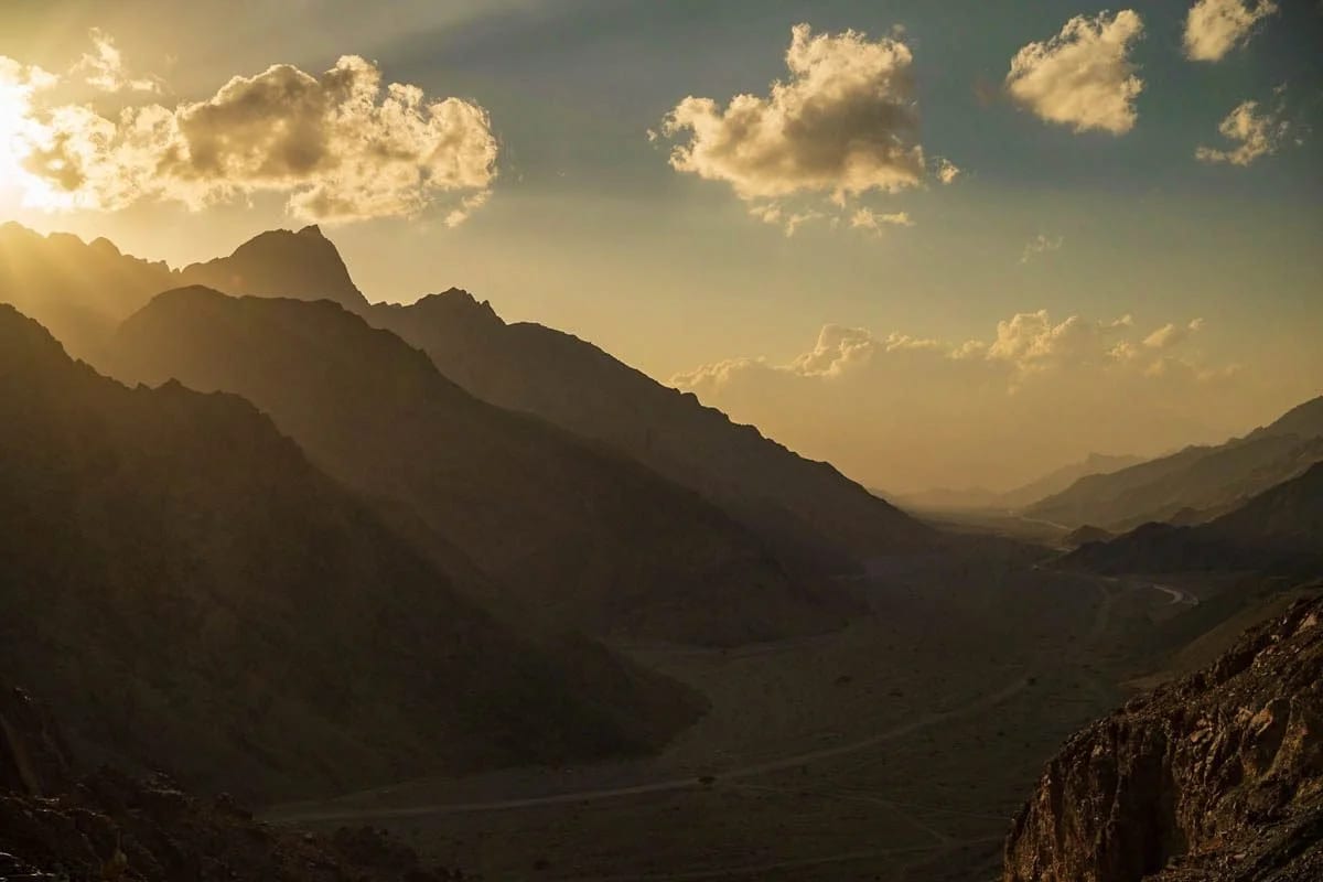 Sunset light through clouds over a rugged mountain valley.