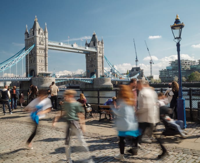 Tower Bridge on a bright day with blurred pedestrians crossing a cobbled riverside walk.
