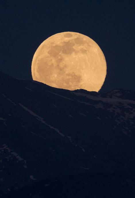 A full moon rising behind a dark mountain ridge.
