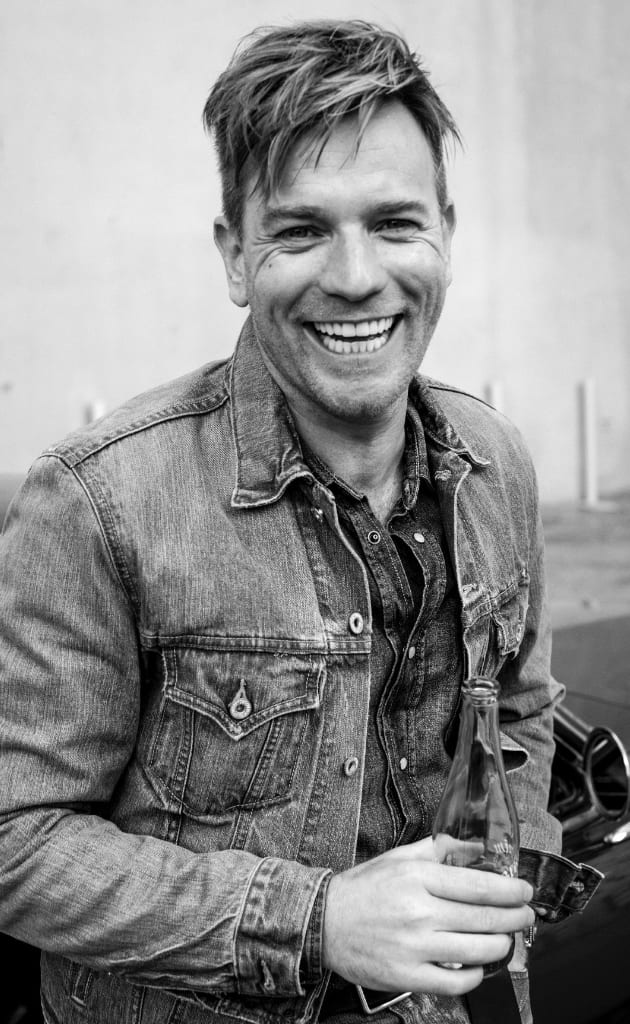 Black and white photograph of Ewan McGregor laughing in a denim jacket.
