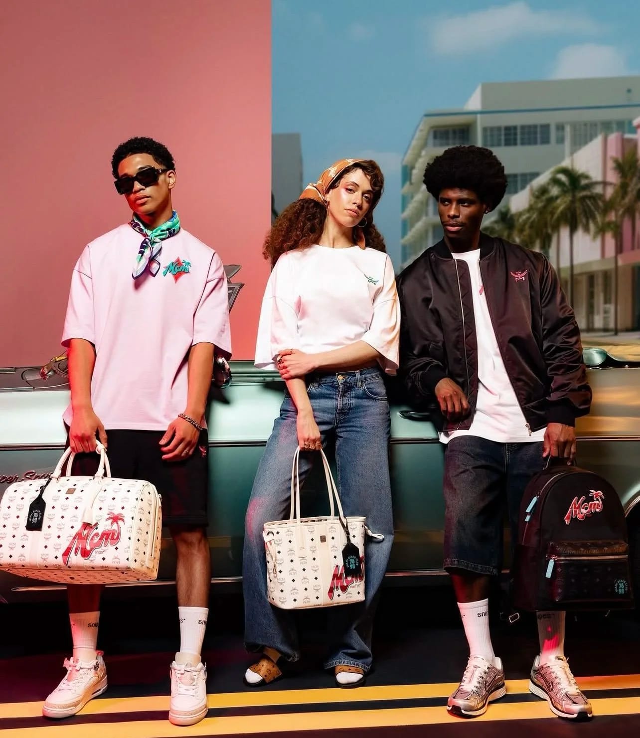 Three young people in pastel streetwear leaning on a green convertible with monogrammed bags, pink buildings behind.