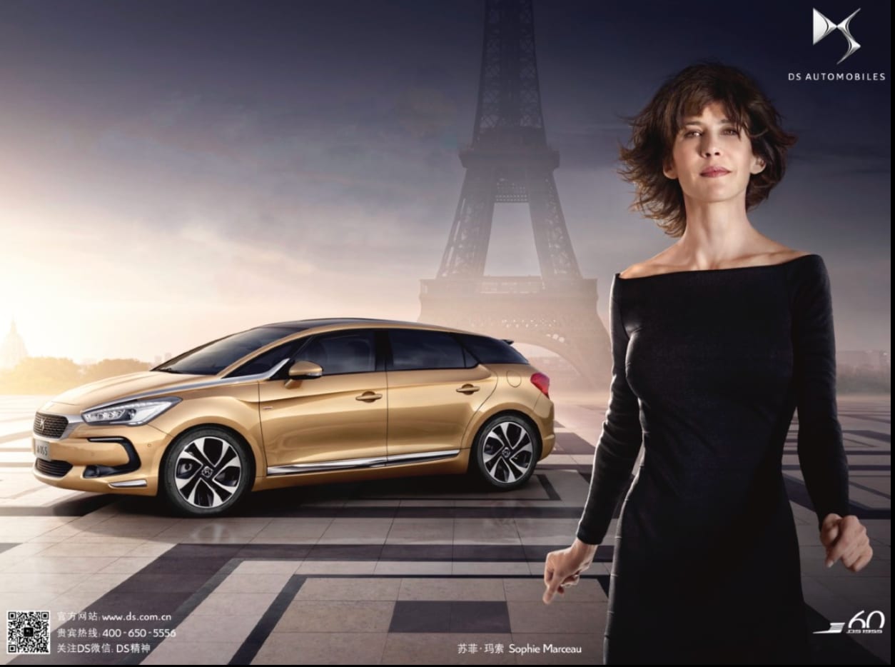 DS Automobiles advertisement: a woman in a black dress beside a gold hatchback in front of the Eiffel Tower.