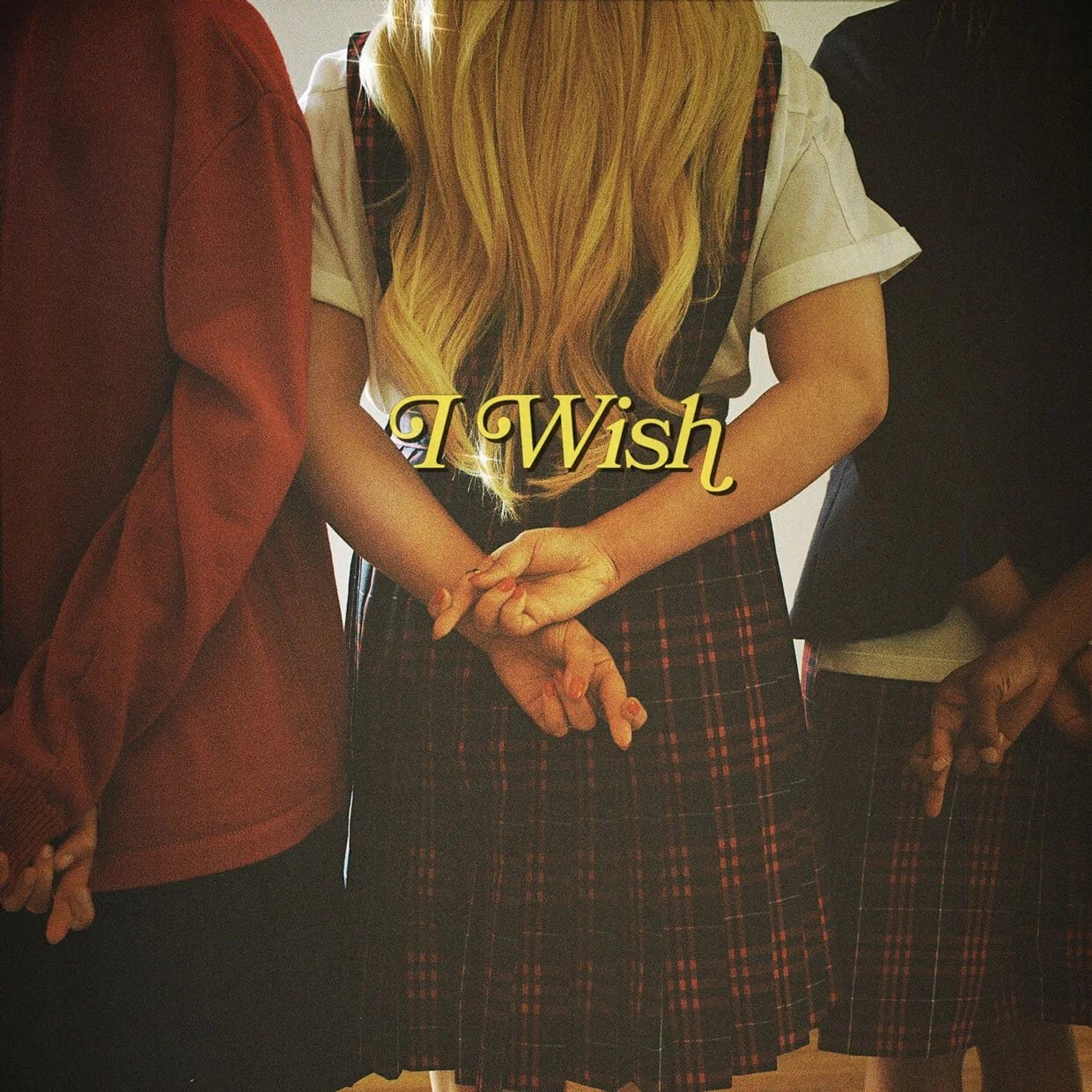 A blonde woman in a plaid skirt seen from behind, holding hands with two people either side, with the words I wish in gold script.