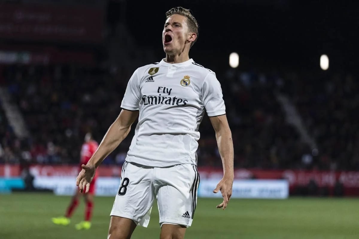 A footballer in a white Fly Emirates shirt shouting with his arms spread under floodlights.