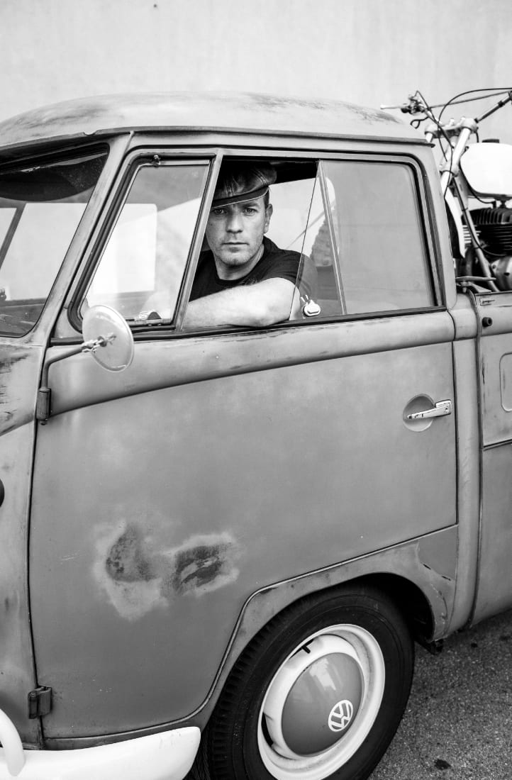 Black and white photograph of Ewan McGregor looking out of the window of a weathered Volkswagen pick-up.