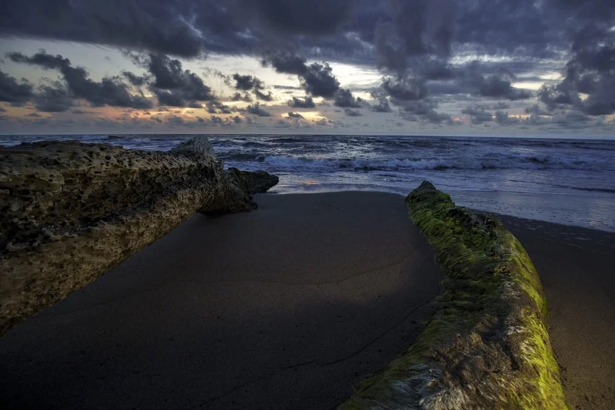 A dark stone jetty running out into the sea under a heavy sky at dusk.