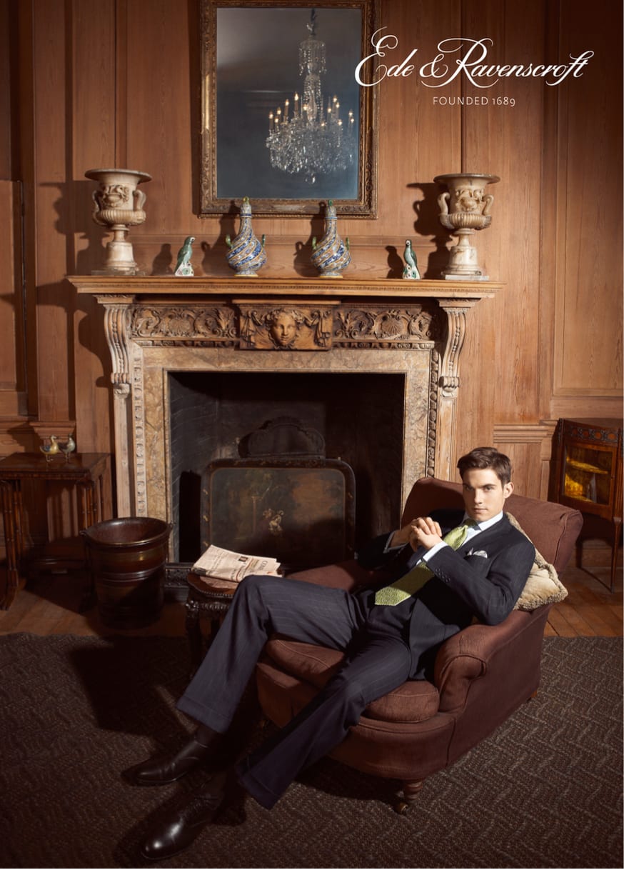 Ede and Ravenscroft advertisement: a man in a navy suit reclining in a leather armchair beside a carved fireplace.