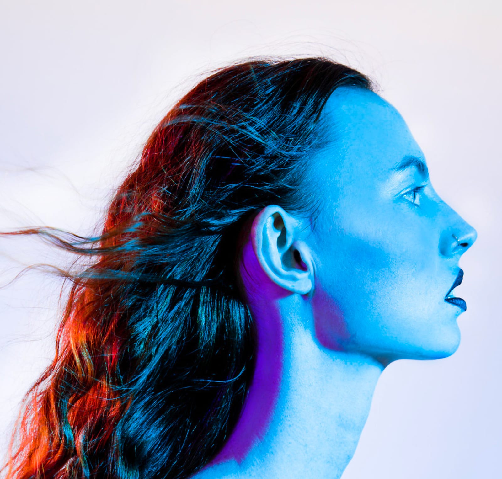 Profile of a woman lit blue and red, her hair streaming back, against white.