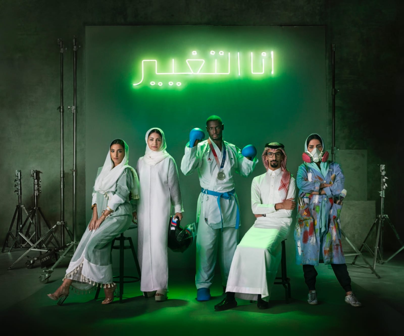 Five people in white, including a boxer with a medal, seated beneath a green neon sign in Arabic in a studio.