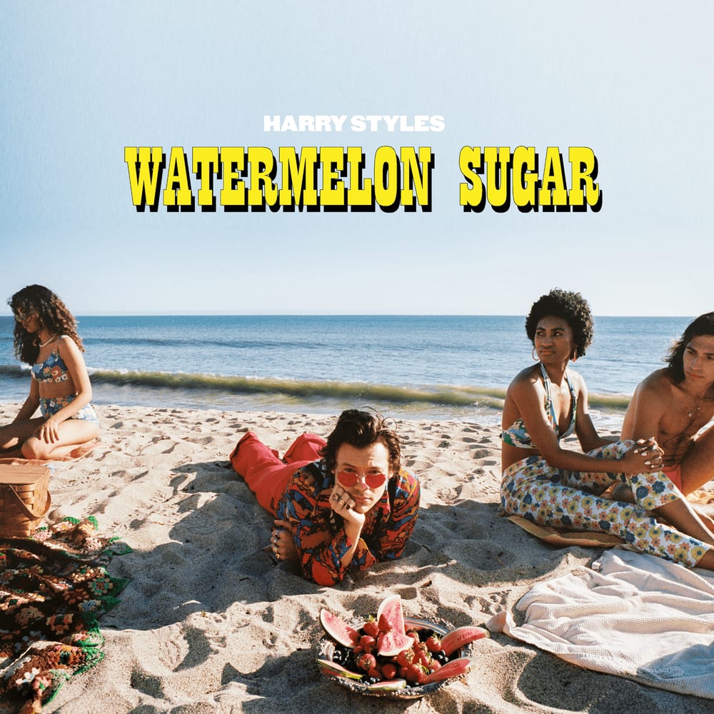 Album cover reading Harry Styles Watermelon Sugar: Harry lies on the sand in a red shirt among a group in swimwear, a plate of watermelon beside them.