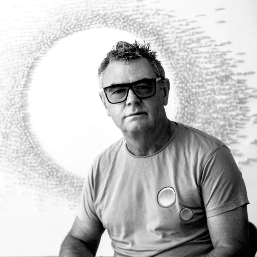 Black and white portrait of Howard Greenhalgh in sunglasses and a T-shirt against a halo of light and scattered marks.