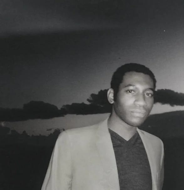 Grainy black and white photograph of Munachi Osegbu in a pale jacket in front of a lake at dusk.