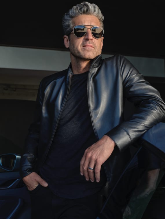 A grey-haired man in aviator sunglasses and a black leather jacket, one hand in his pocket.