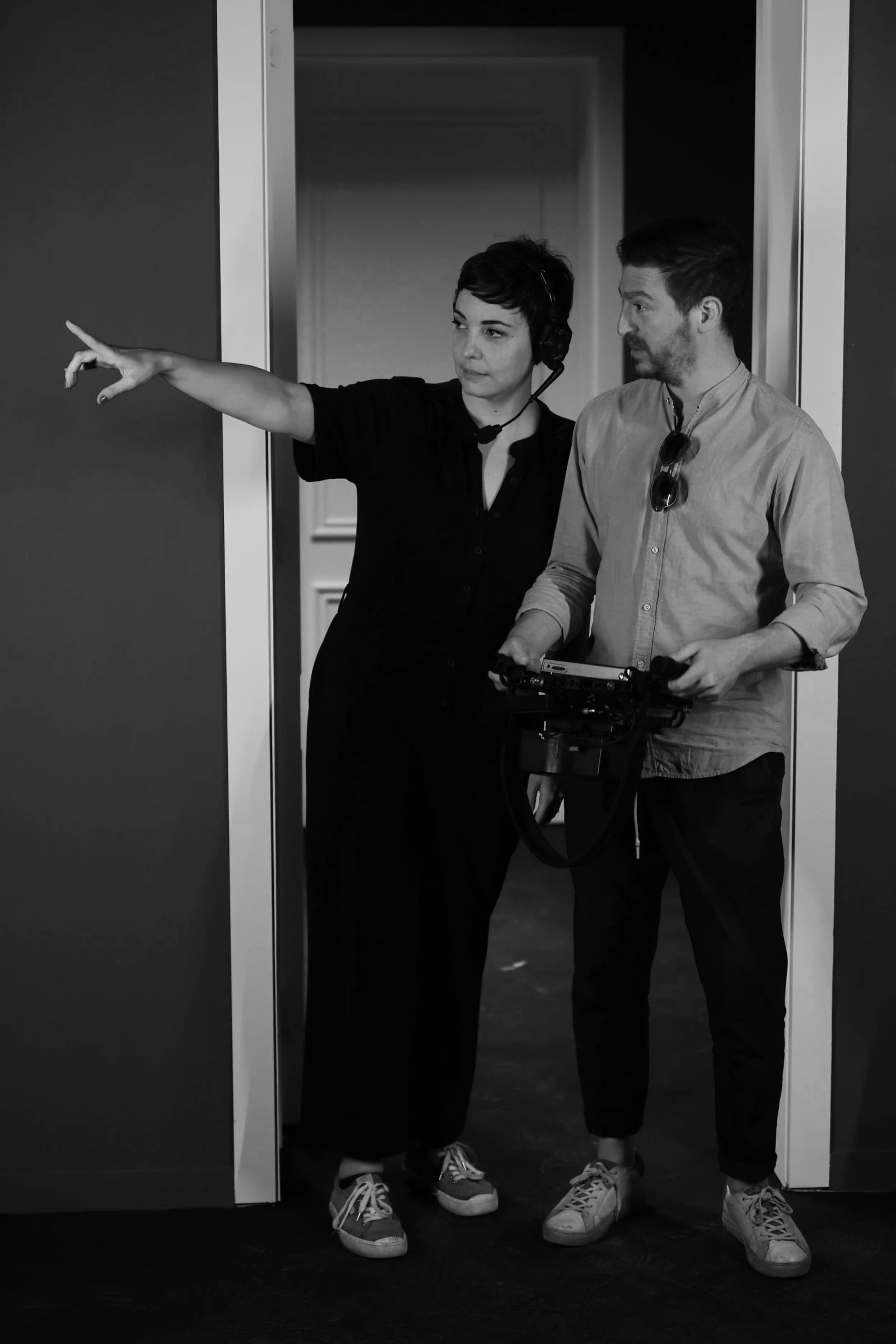 Black and white photograph of Giacomo Calistri and Laura Innocenti in a doorway, Laura pointing off to the left, Giacomo holding a camera.
