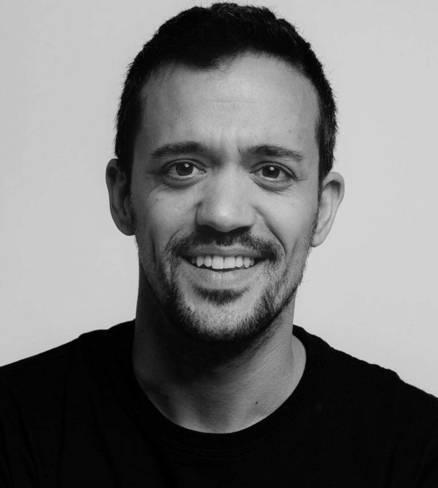 Black and white portrait of Joan Gosa smiling in a black T-shirt.