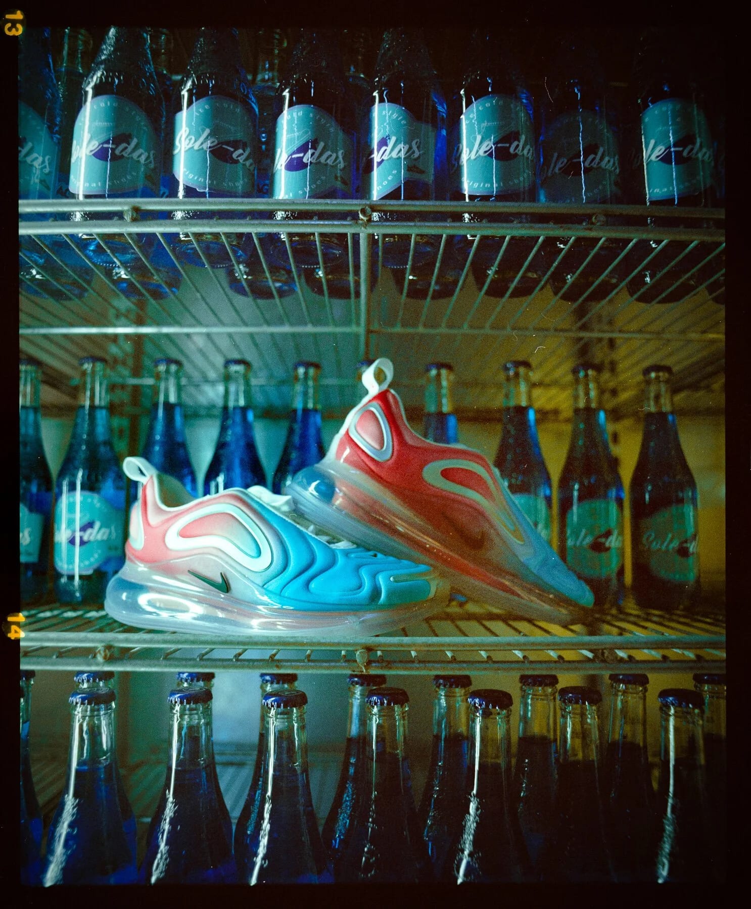 A pink and blue Nike Air trainer sitting on a shelf inside a drinks fridge between rows of glass bottles.