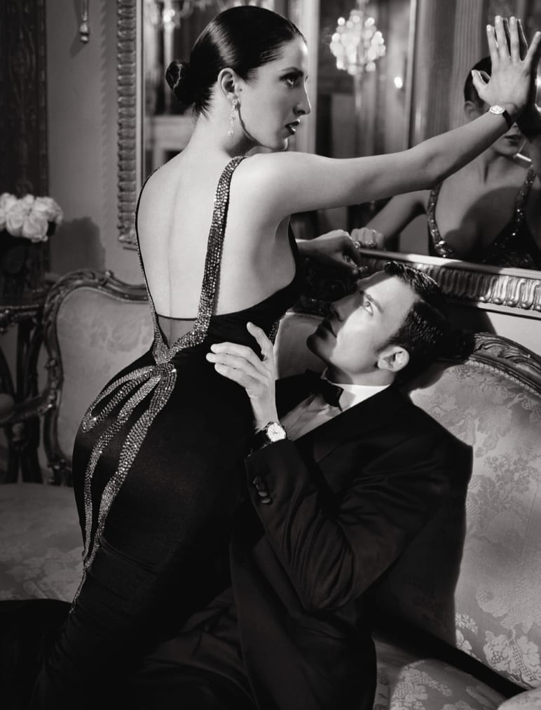 Black and white photograph of a woman in a backless sequinned gown embracing a man in a tuxedo in an ornate room.