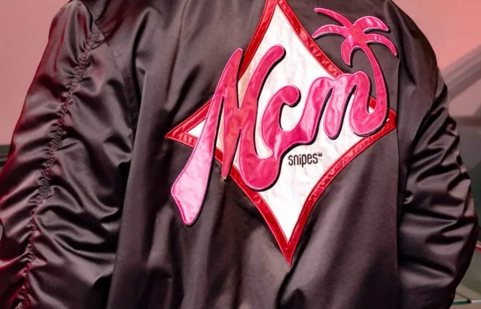 Close-up of a black satin bomber jacket with a pink MCM diamond patch on the back.