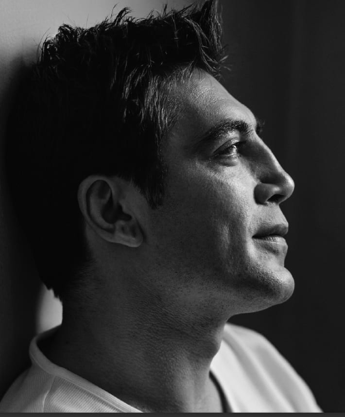 Black and white profile of a dark-haired man in a white T-shirt looking to the right in low light.