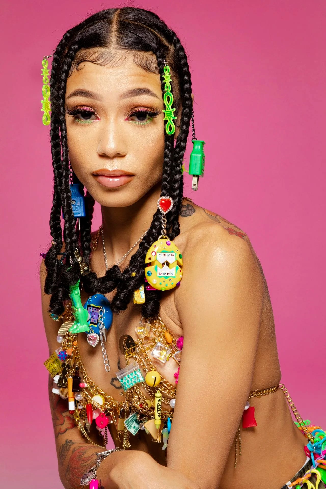 A young woman with beaded braids wearing layered charm necklaces against pink.