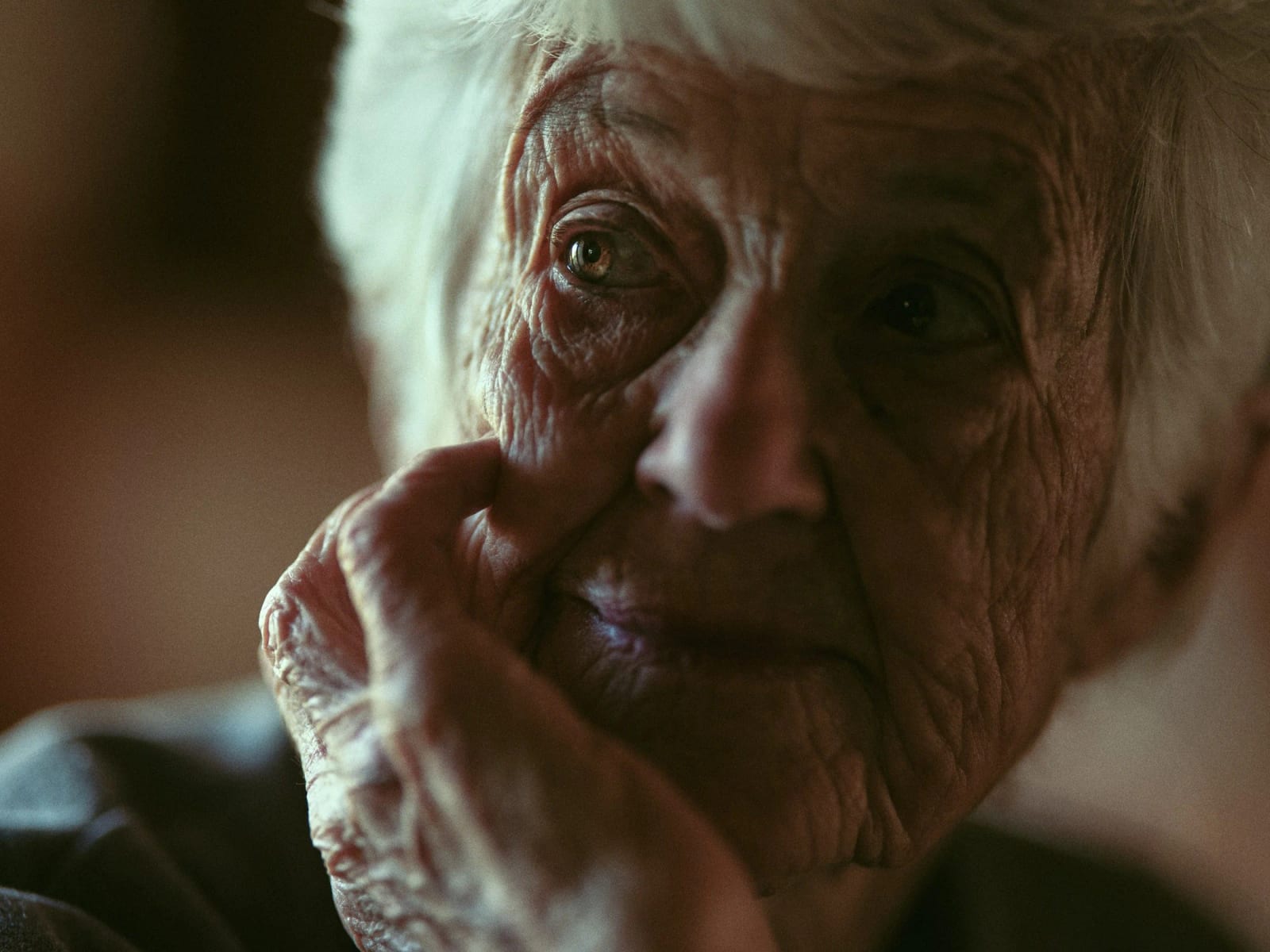 Close-up of an elderly white-haired woman resting her chin on her hand, looking off to the side.