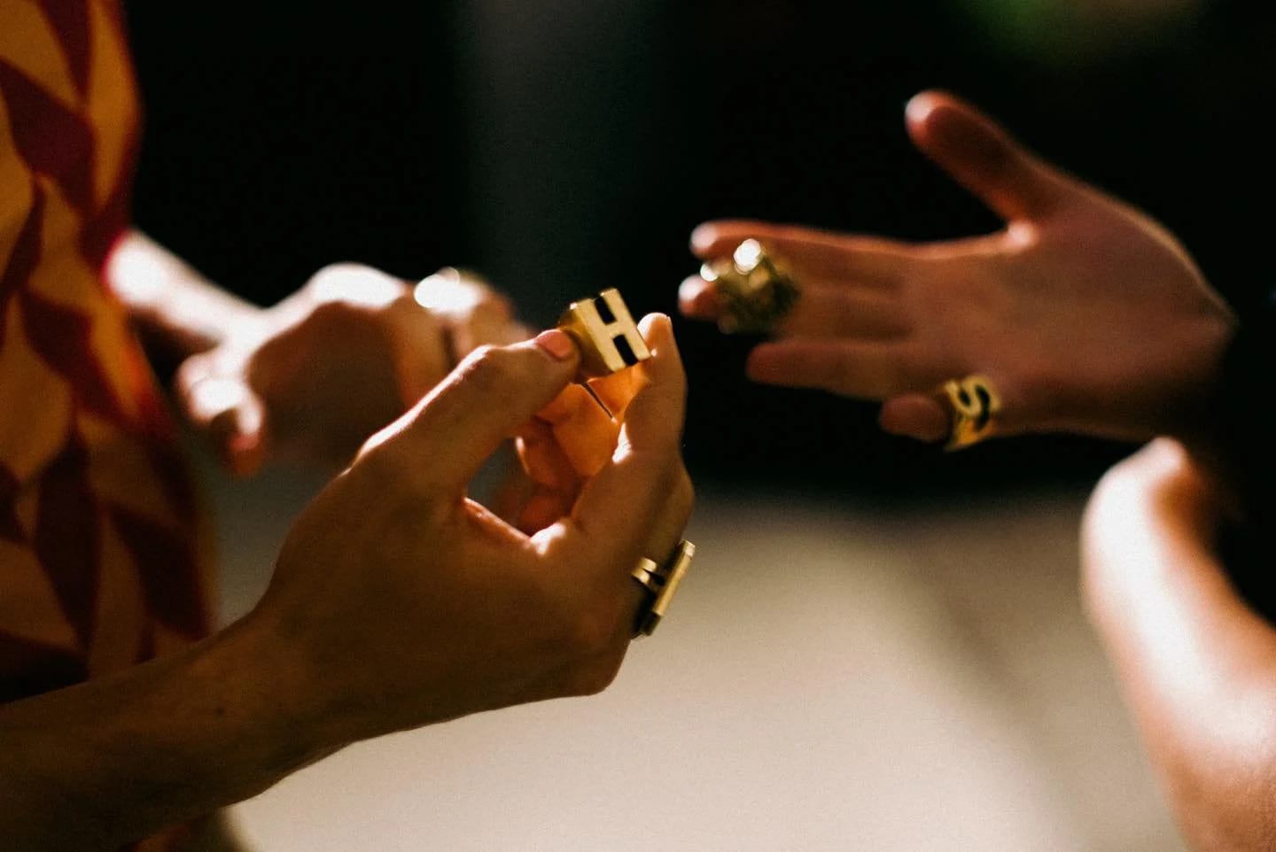 Close-up of ringed hands passing a small gold object from one to the other under warm light.