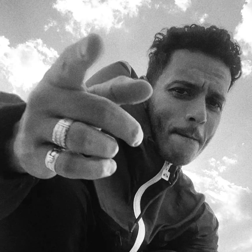 Black and white photograph of Mohammed Hammad pointing a ringed finger at the camera against a cloudy sky.