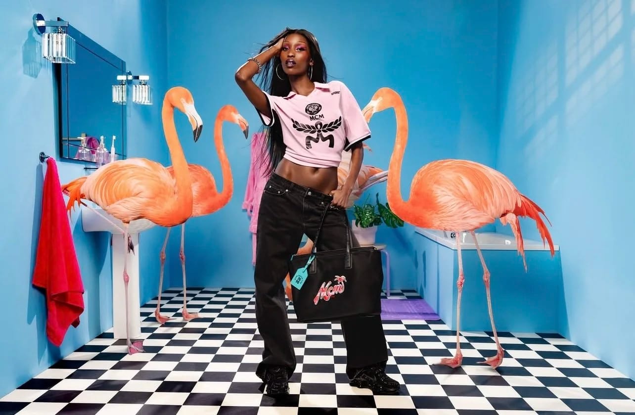 A woman in a pink T-shirt and black trousers posing in a blue bathroom set between two flamingo models.