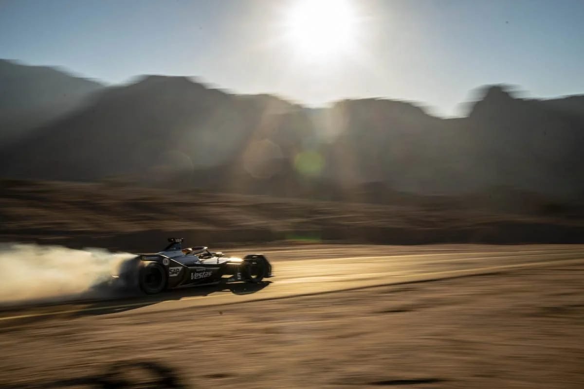 A racing car speeding across a desert track against a low sun, blurred by motion.