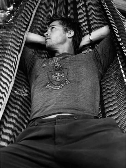 Black and white photograph of a man lying back in a hammock with his hands behind his head, looking upward.